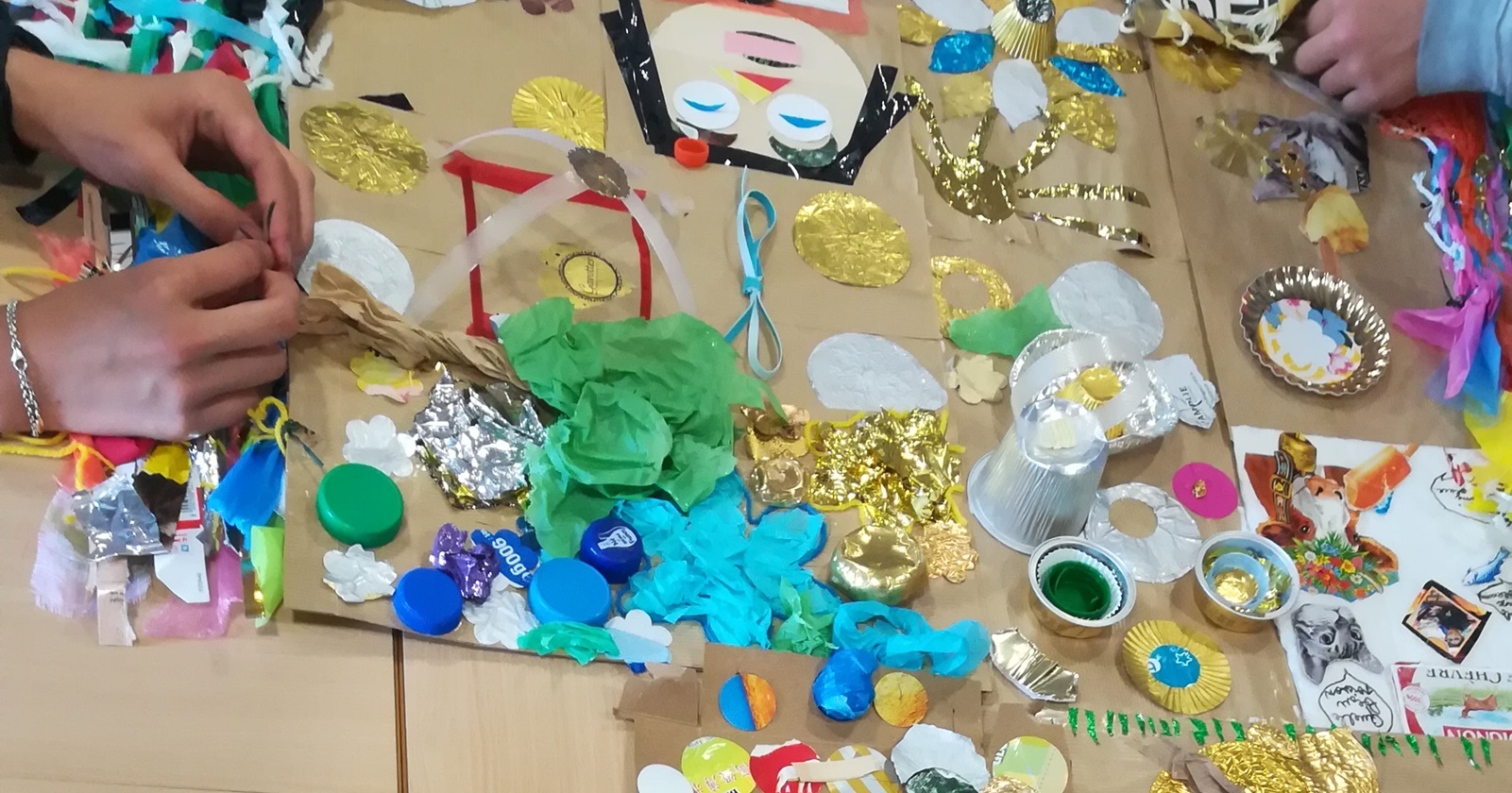 Des mains qui sont en train de créer alors que plein de jolis déchets colorés sont posés sur une table.